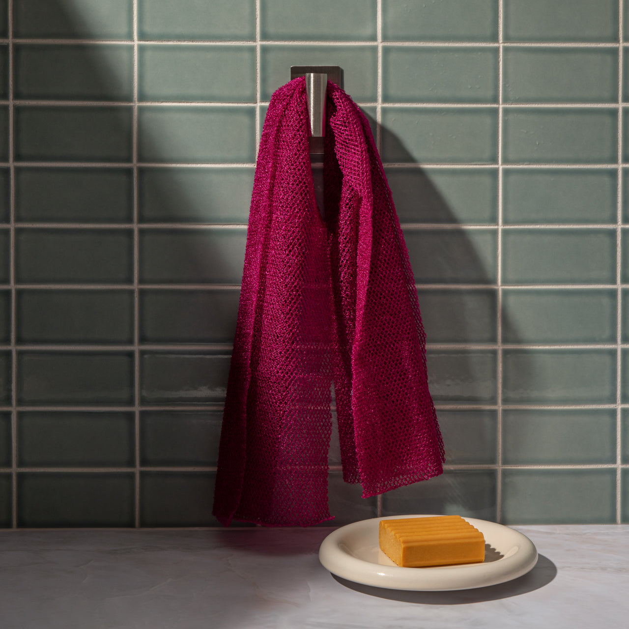 Berry Pink African Net Sponge hanging in a bathroom setting beside a sink, showcasing its long reusable body scrub design.