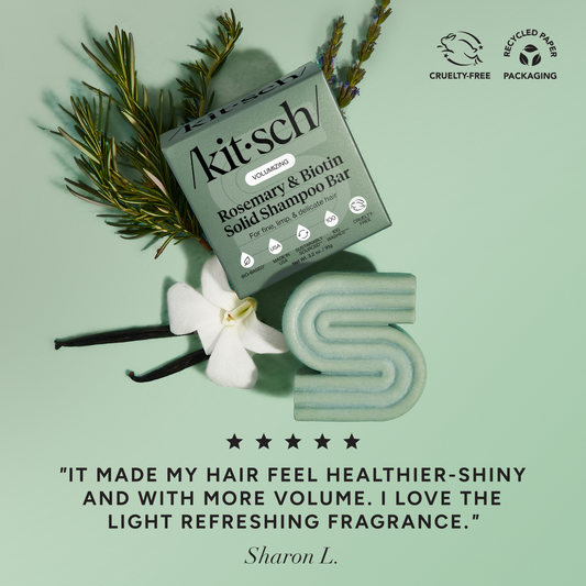 5-star customer review flat-lay for KITSCH Volumizing Rosemary & Biotin Solid Shampoo Bar on sage green background styled with rosemary sprigs, white flower, and vanilla beans — Sharon L.: "IT MADE MY HAIR FEEL HEALTHIER-SHINY AND WITH MORE VOLUME. I LOVE THE LIGHT REFRESHING FRAGRANCE." — Cruelty-Free, Recycled Paper Packaging