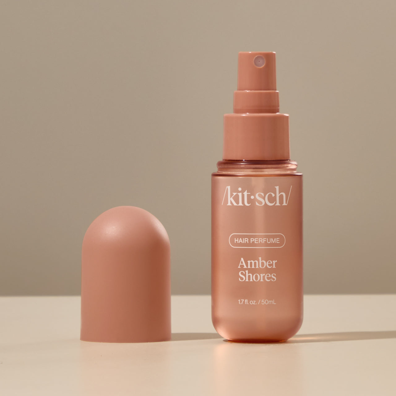 Kitsch Amber Shores Hair Perfume bottle held by a hand against a warm neutral background