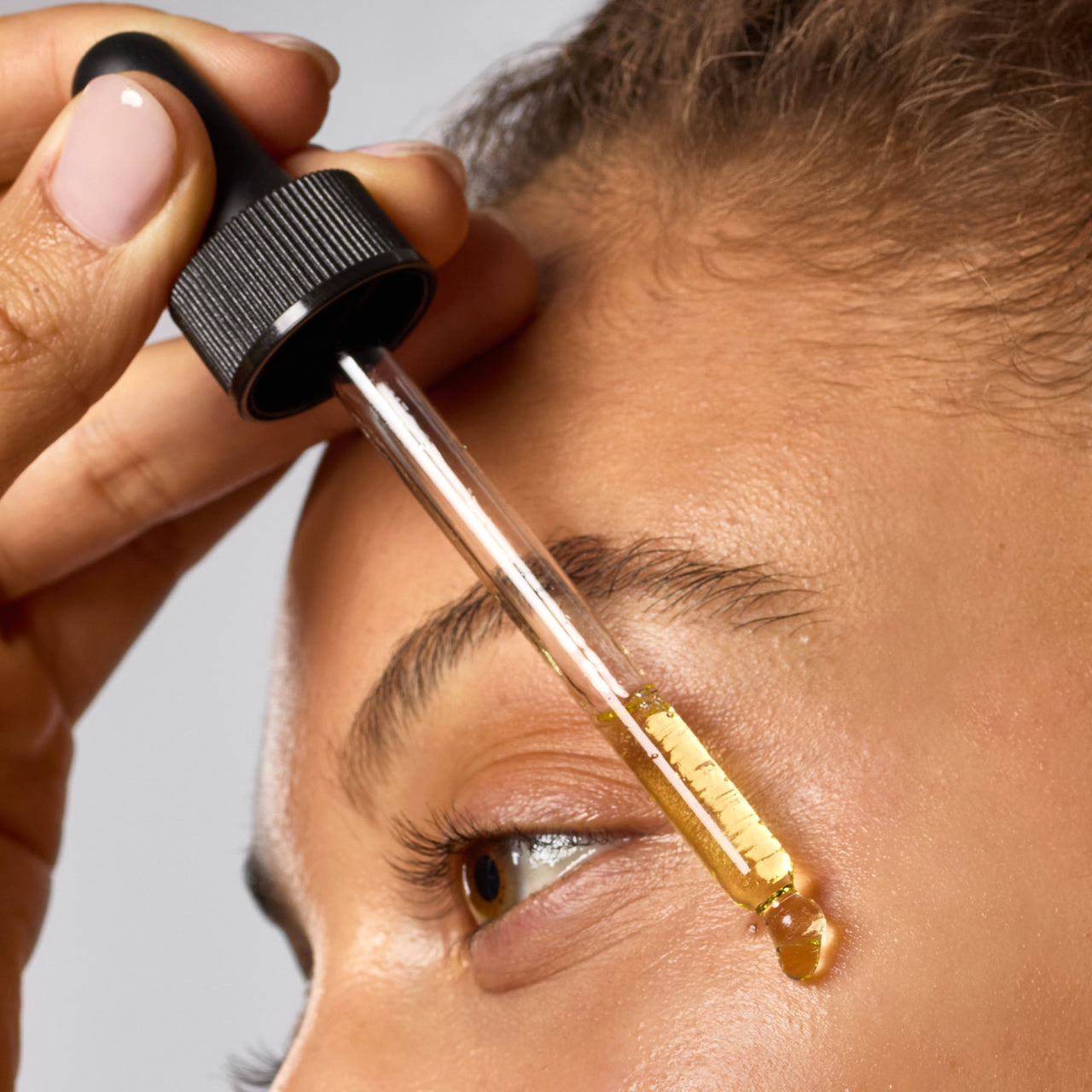 Close-up view of Hydrating Dermaplane Oil being applied to facial skin with a dropper.