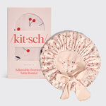 Pink satin bonnet with cherry pattern next to its packaging box on a light gray background