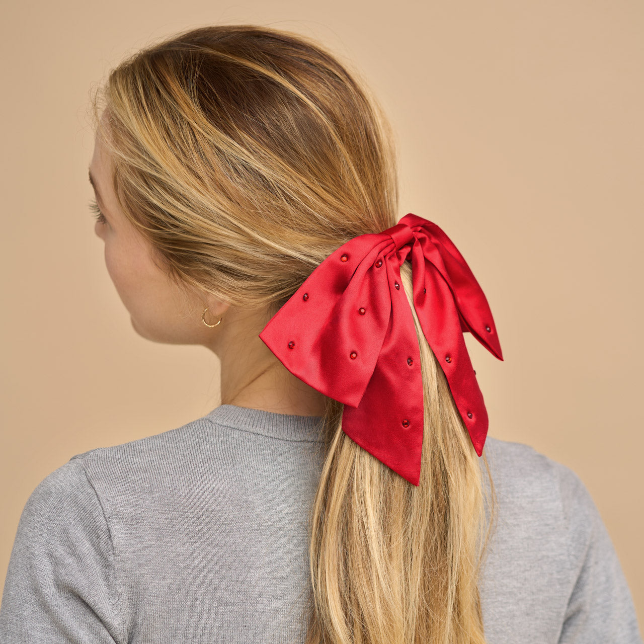 KITSCH Satin & Rhinestone Bow Scrunchie — model styling hair with rhinestone bow scrunchie — festive red satin with rhinestone bow for holiday looks — gentle on all hair types