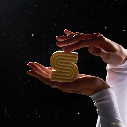 Hands cradling KITSCH x Star Wars™ honey-gold S-shaped Rice Water Protein Solid Shampoo Bar (C-3PO edition) against dark galaxy starfield backdrop — unboxed bar lifestyle product shot for Strengthening formula For thin, fine, & damaged hair