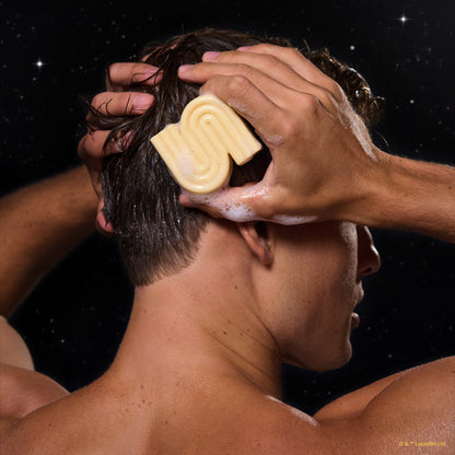 Back view of male model applying lathered KITSCH x Star Wars™ honey-gold S-shaped Rice Water Protein Solid Shampoo Bar (C-3PO edition) to wet dark hair — lifestyle in-use shot against galaxy starfield backdrop — Strengthening formula For thin, fine, & damaged hair