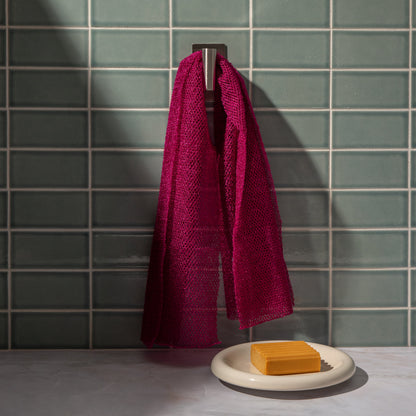 Berry Pink African Net Sponge hanging in a bathroom setting beside a sink, showcasing its long reusable body scrub design.