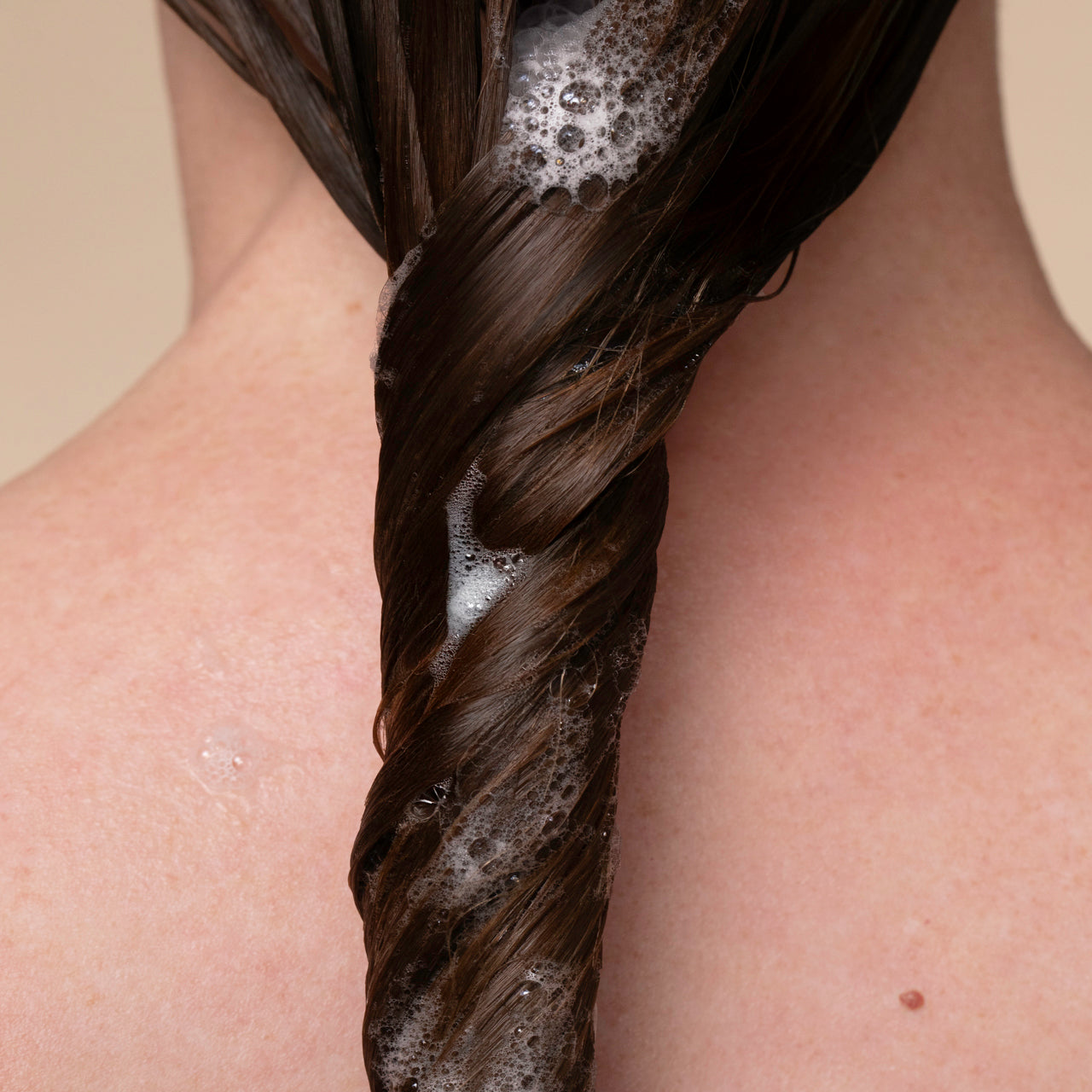 Person lathering KITSCH Smoothing Castor Oil Shampoo into hair, showing rich lather on a beige background