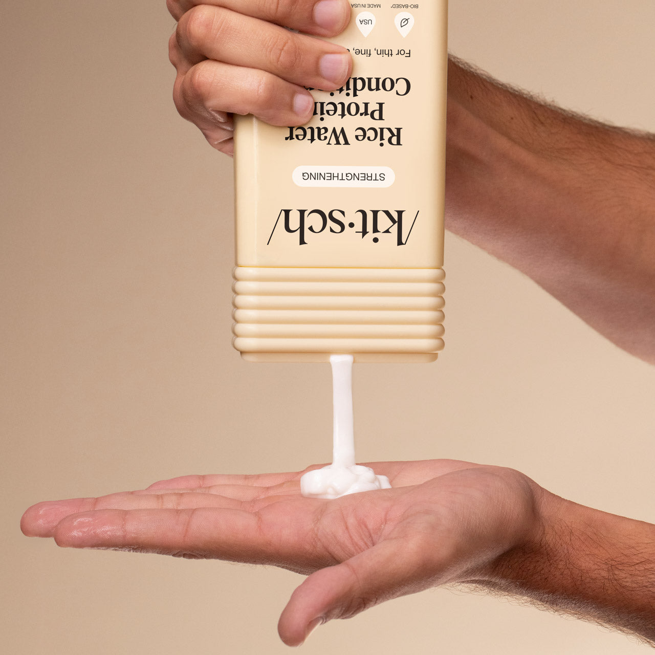 Hand dispensing KITSCH Rice Water Protein Strengthening Conditioner from bottle into palm on a beige background