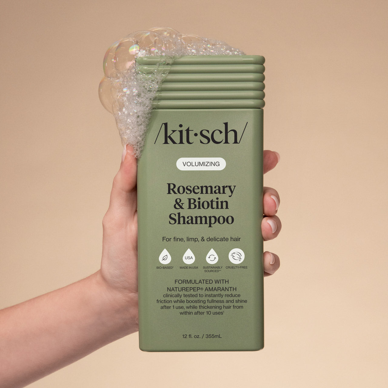 Kitsch Rosemary & Biotin Shampoo bottle held by a hand against a beige background