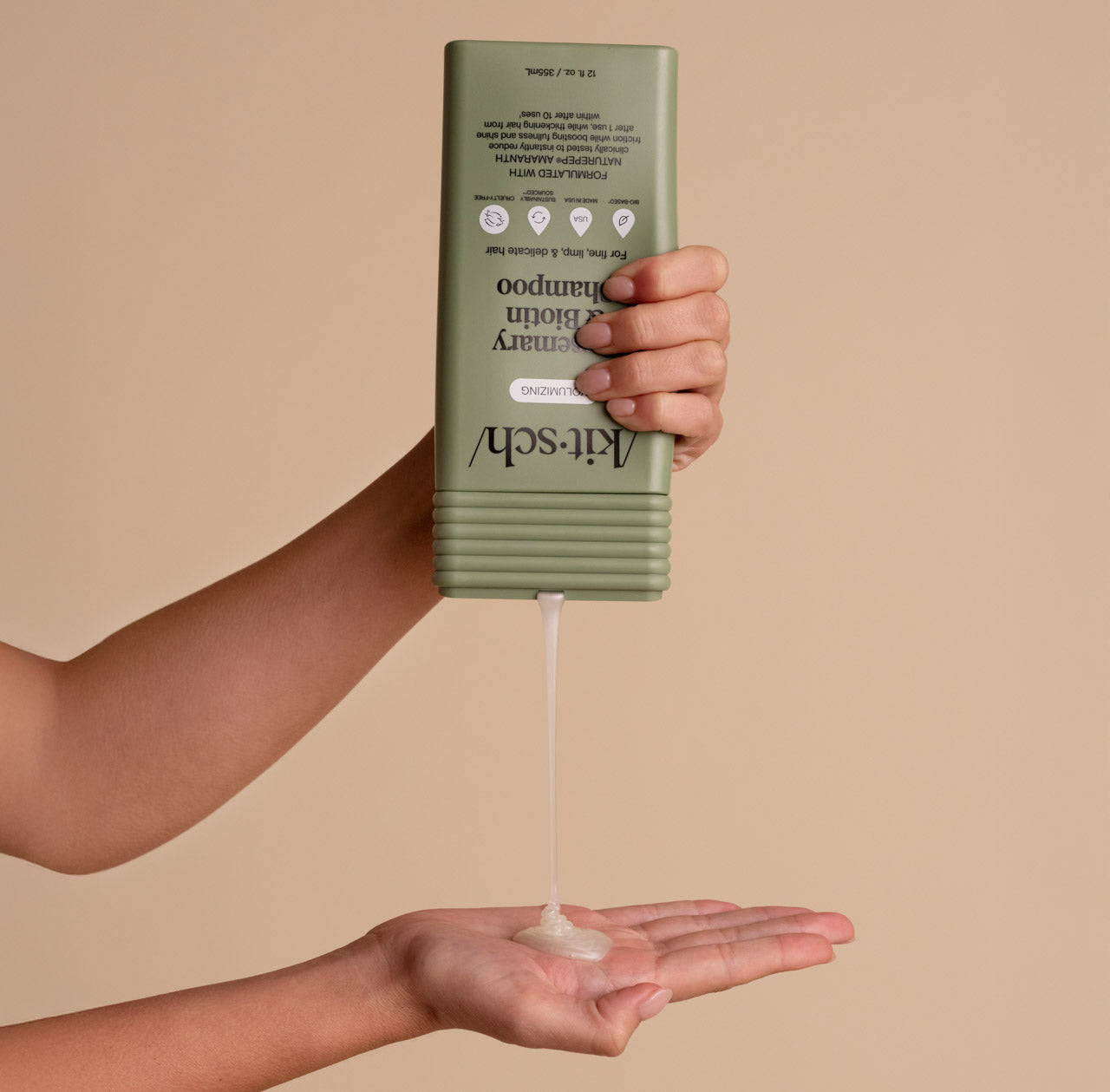 Hand holding a green shampoo bottle with pump dispensing shampoo into another hand against a beige background