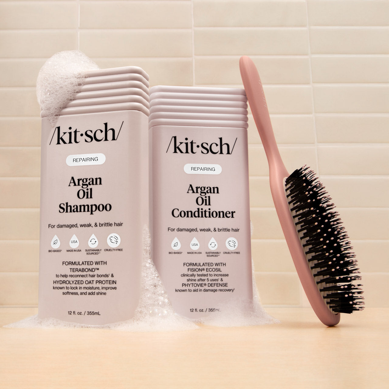 KITSCH Repairing Argan Oil Shampoo and Conditioner 12 fl. oz. bottles styled alongside a KITSCH Smooth Polish round brush on tile background — creative product shoot for KITSCH Repairing Argan Oil collection for damaged, weak, & brittle hair