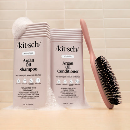 KITSCH Repairing Argan Oil Shampoo and Conditioner 12 fl. oz. bottles styled alongside a KITSCH Smooth Polish round brush on tile background — creative product shoot for KITSCH Repairing Argan Oil collection for damaged, weak, & brittle hair