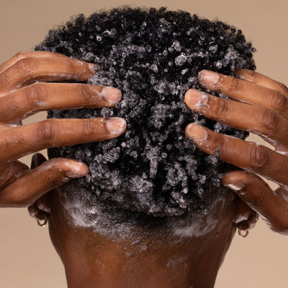 Person massaging KITSCH Coconut Oil Shampoo lather into kinky coily hair, demonstrating how to use