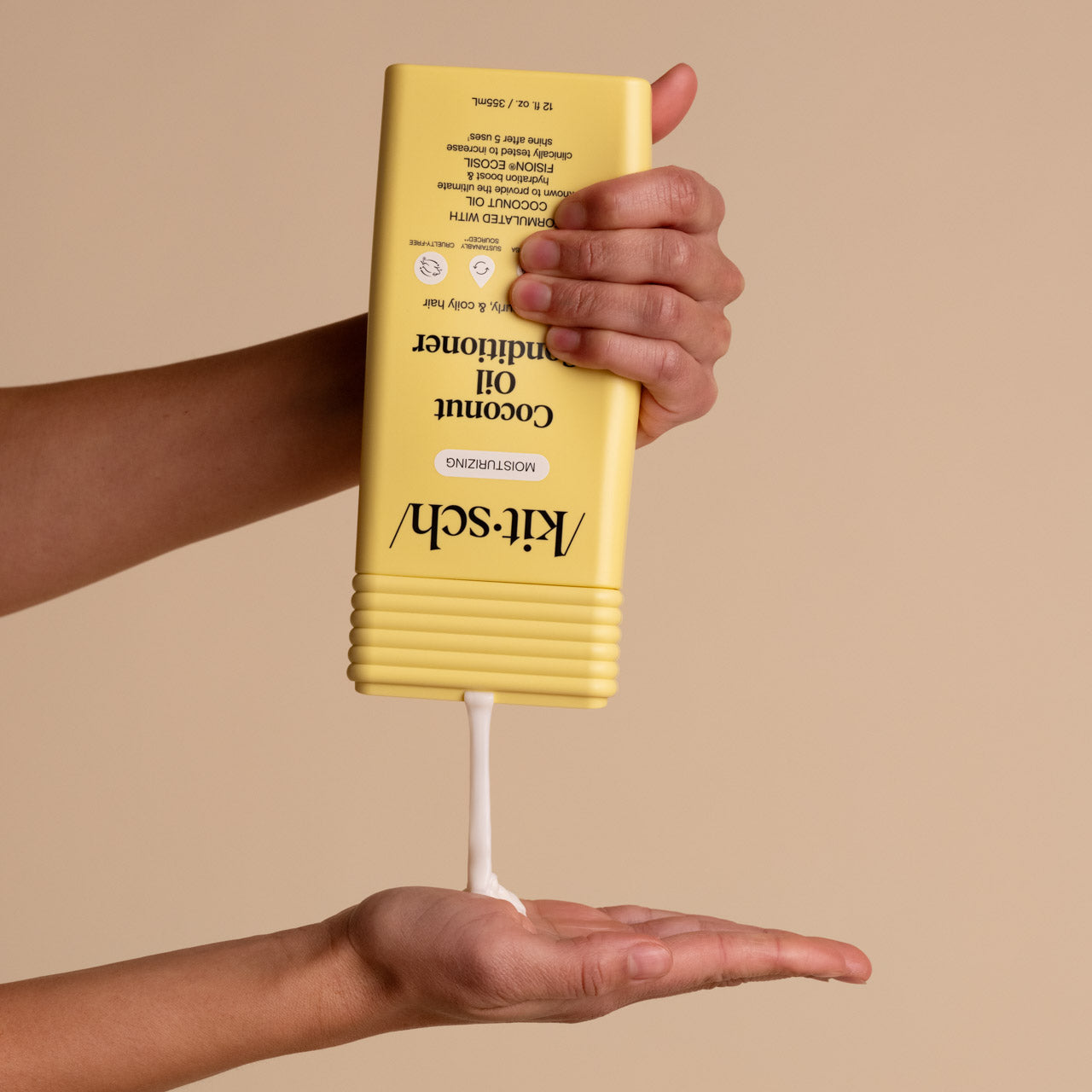 Hand dispensing KITSCH Moisturizing Coconut Oil Conditioner from yellow bottle into palm, beige background