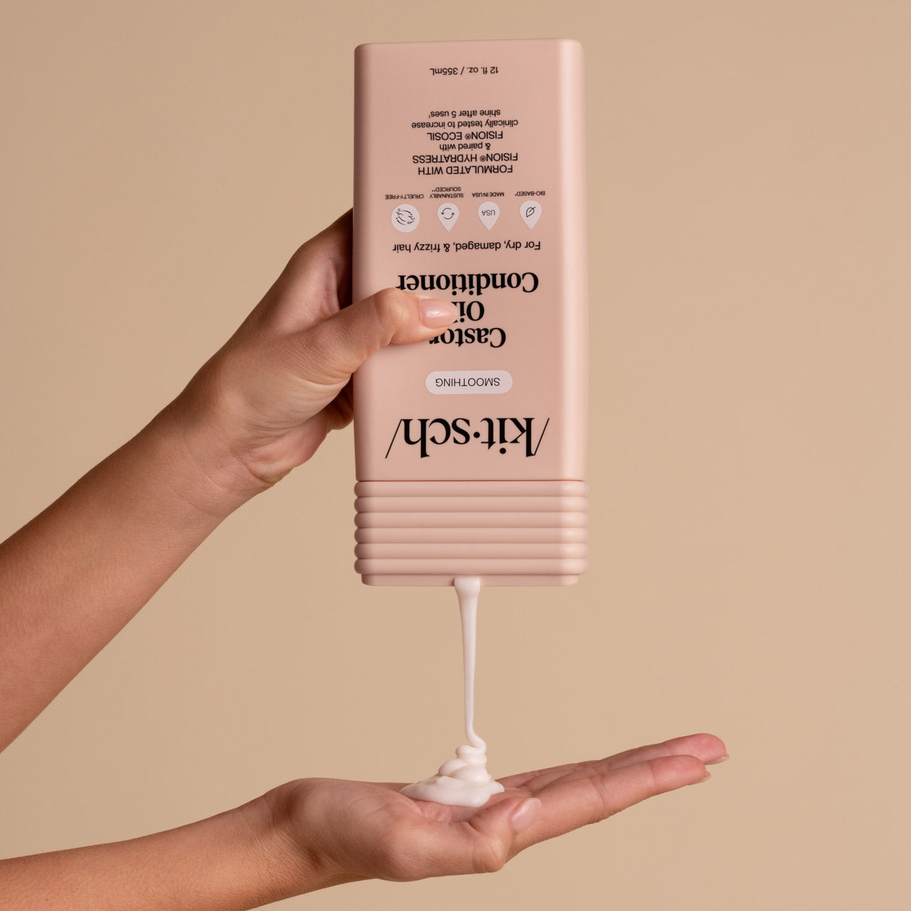 Hand dispensing KITSCH Smoothing Castor Oil Conditioner from bottle into palm on a beige background
