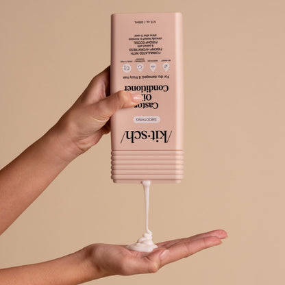 Hand dispensing KITSCH Smoothing Castor Oil Conditioner from bottle into palm on a beige background