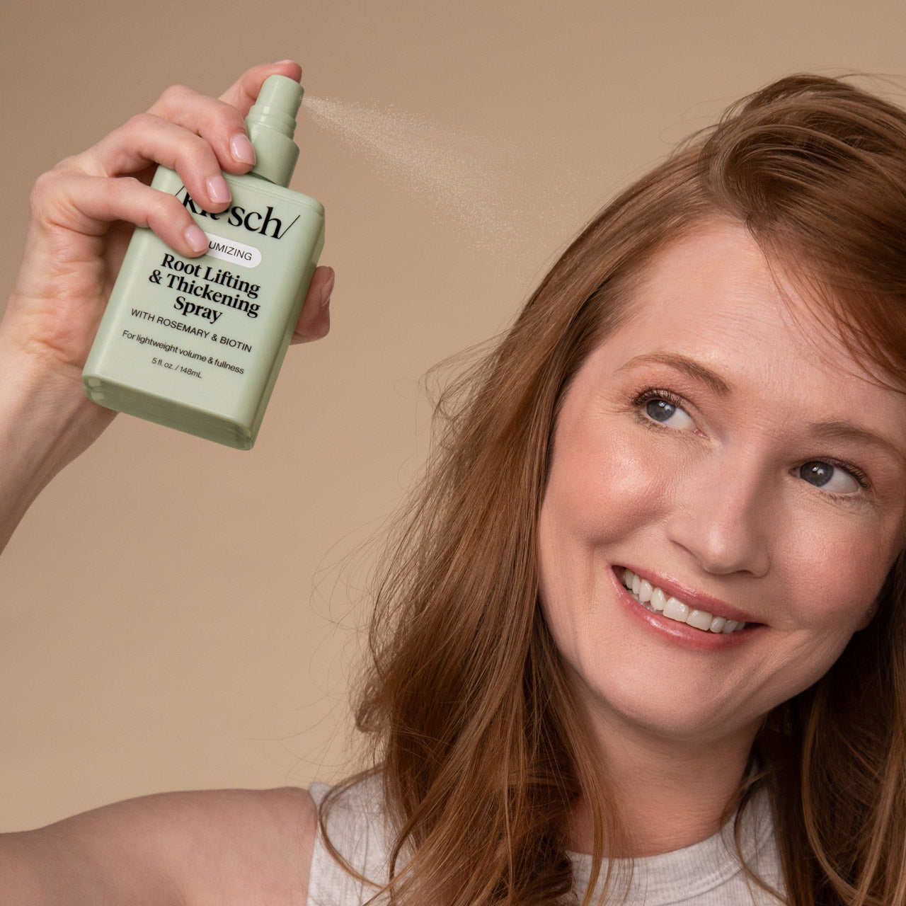 KITSCH Root Lifting & Thickening Spray — lifestyle portrait of female model with long auburn hair, smiling, spraying product at roots, warm beige background — For lightweight volume & fullness at your roots — Infused with rosemary & Biotin to help promote the appearance of healthy hair — 86% agreed provided noticeable lift & volume at roots