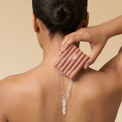 Woman lathering Kitsch Amber Shores Body Wash Bar on her back with sudsy foam on a beige background