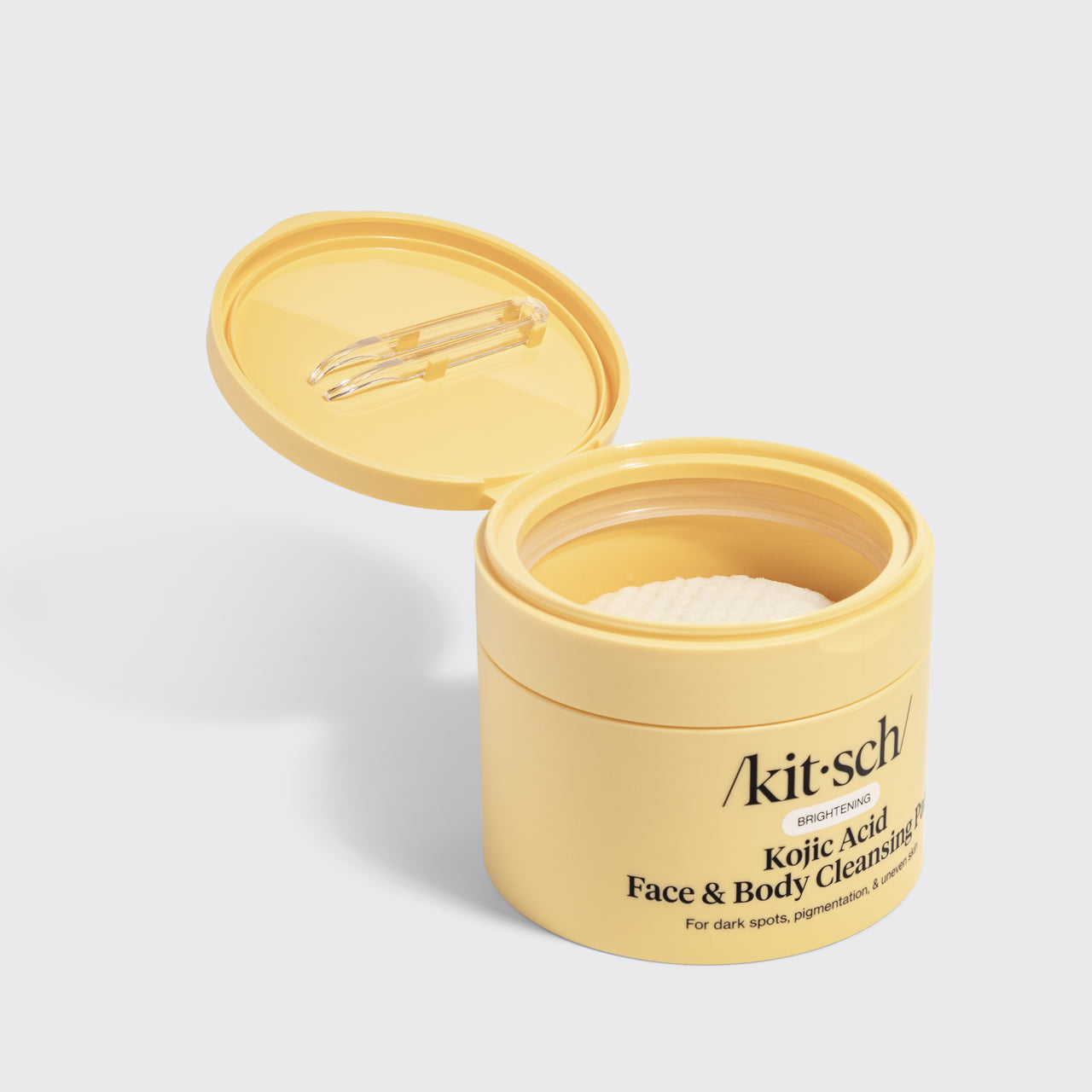 KITSCH Kojic Acid Face & Body Cleansing Pads — open tub product shot on light gray background — yellow jar with lid open showing white pre-soaked pads inside — BRIGHTENING | For dark spots, pigmentation, & uneven skin — Kojic Acid helps fade dark spots, reduce sun damage, and lighten acne scars — Supports elasticity and reduces fine lines — Contains 50 pads