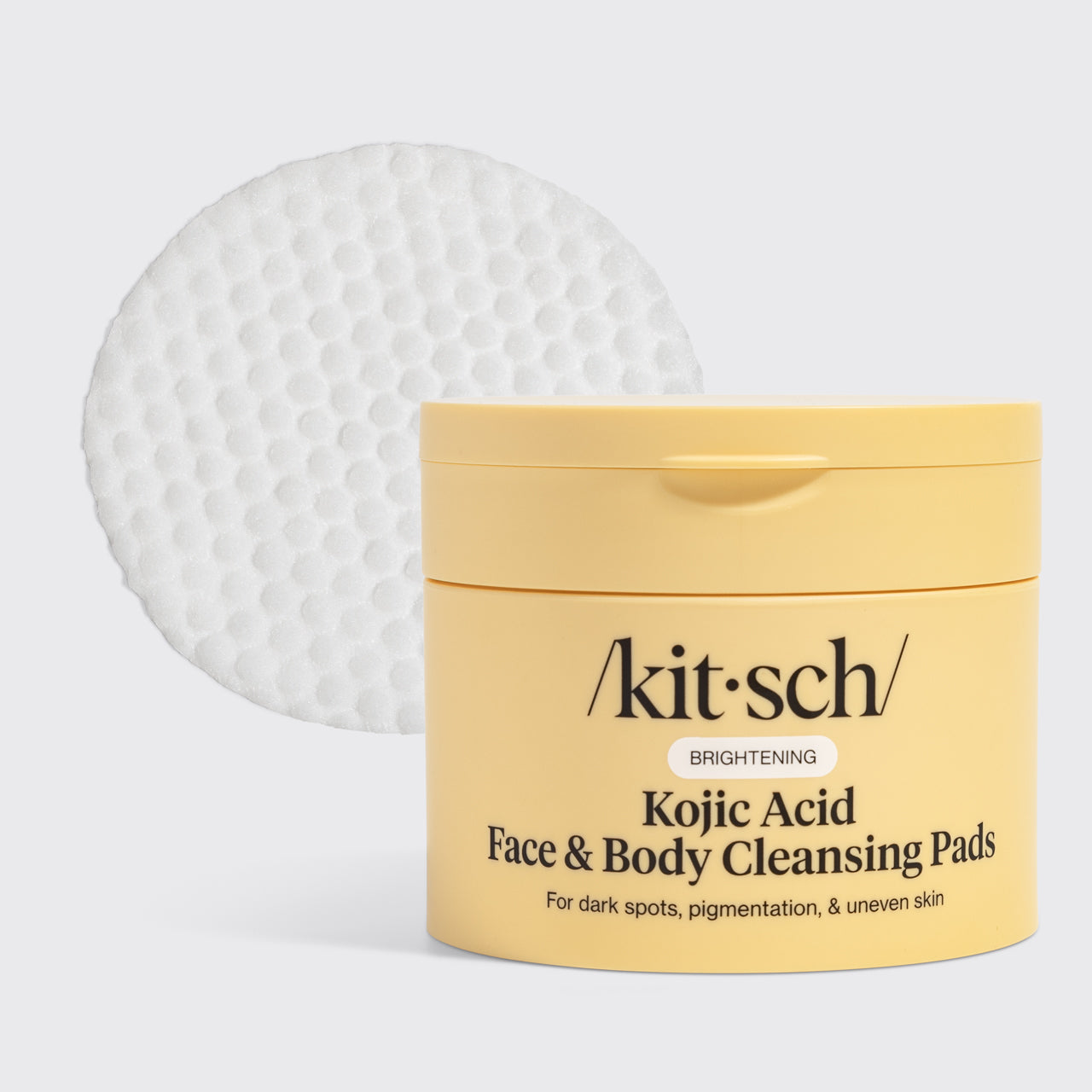 KITSCH Kojic Acid Face & Body Cleansing Pads — hero product shot on light gray background — yellow tub with single white pad displayed — BRIGHTENING | For dark spots, pigmentation, & uneven skin — Kojic Acid helps fade dark spots, reduce sun damage, and lighten acne scars — Turmeric Root Powder fights dullness and boosts antioxidants — Contains 50 pads