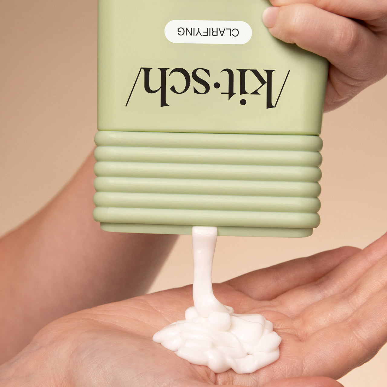 Hand dispensing KITSCH Clarifying Tea Tree & Mint Conditioner from bottle on a beige background