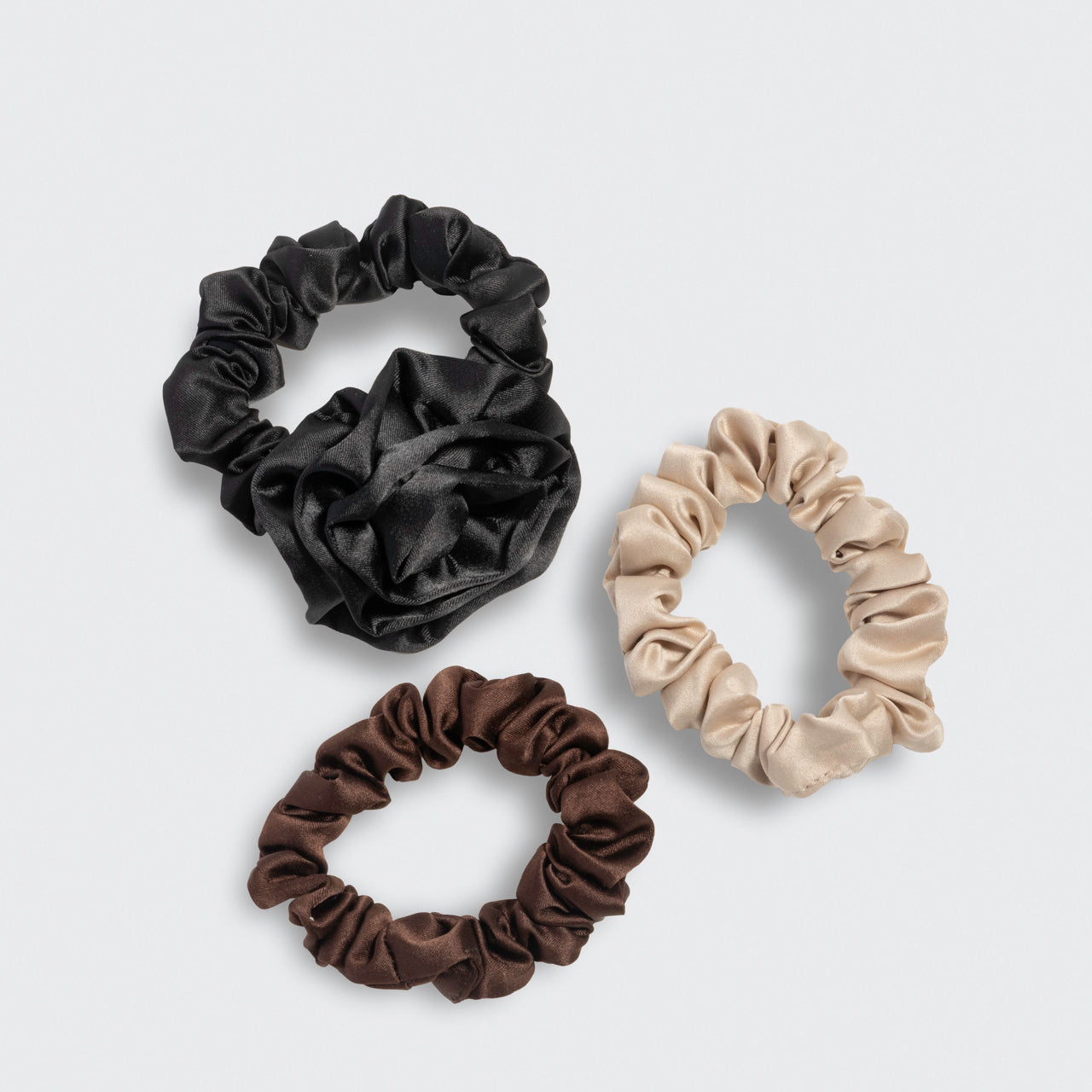 Three scrunchies with the black rosette and brown and cream ruched scrunchies on a light gray background