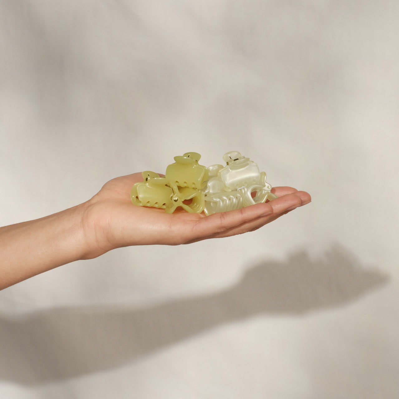 Open palm holding a collection of KITSCH Pearlized Cream & Butter Yellow Jelly Cloud Clips Mini — product showcase shot on cream background — mix of butter yellow & pearlized cream mini jelly claw clips cupped in hand — All-Day Hold | 8pcs, Made from Recycled Materials