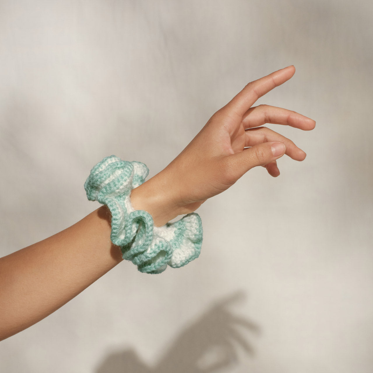 Model wearing KITSCH Coastal Cottage Crochet Scrunchie on wrist, styled in sage green and white against a neutral background