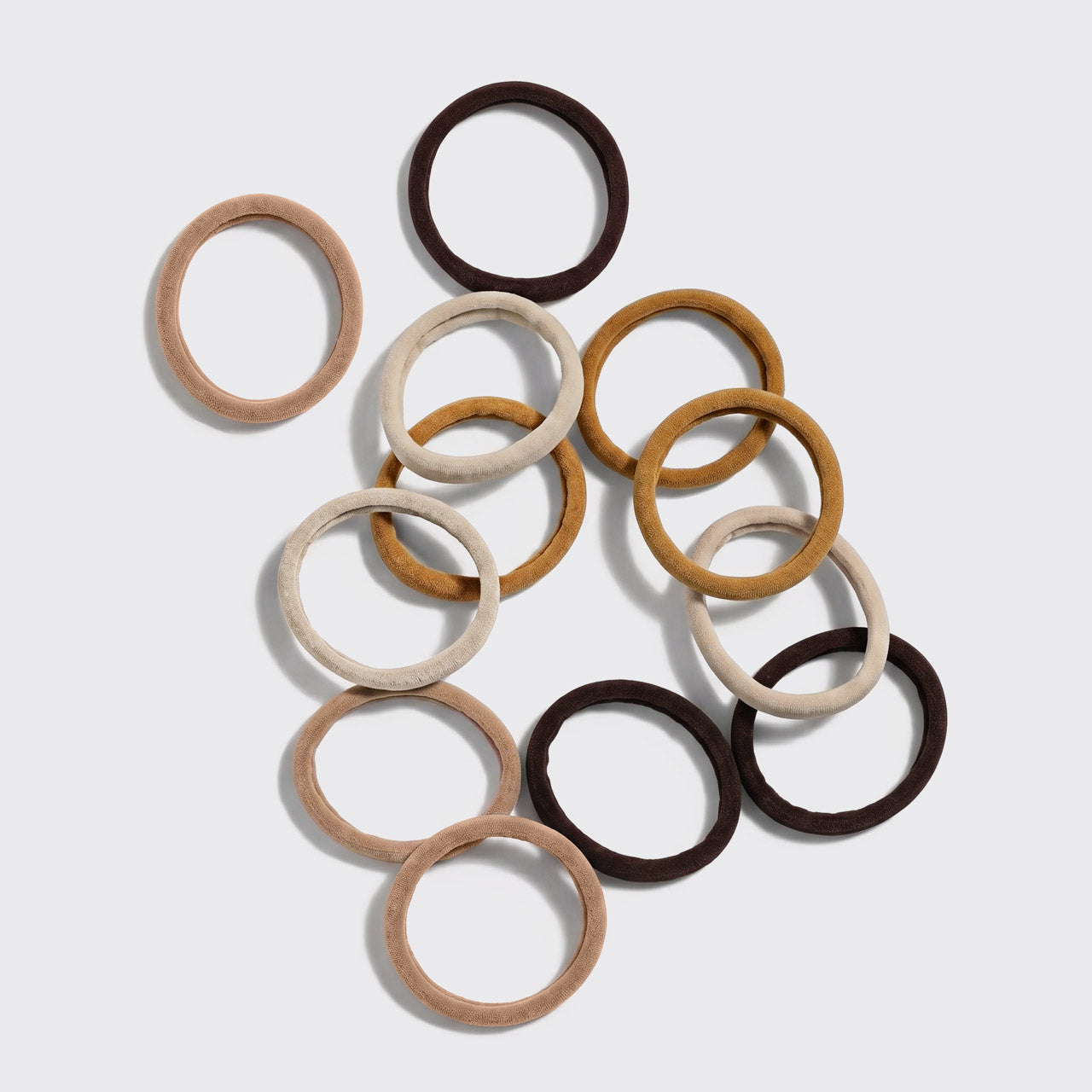 Sedona Seamless Hair Elastics 12pc Set - 12 seamless recycled nylon hair elastics in cream, mustard, and dark brown scattered on grey background