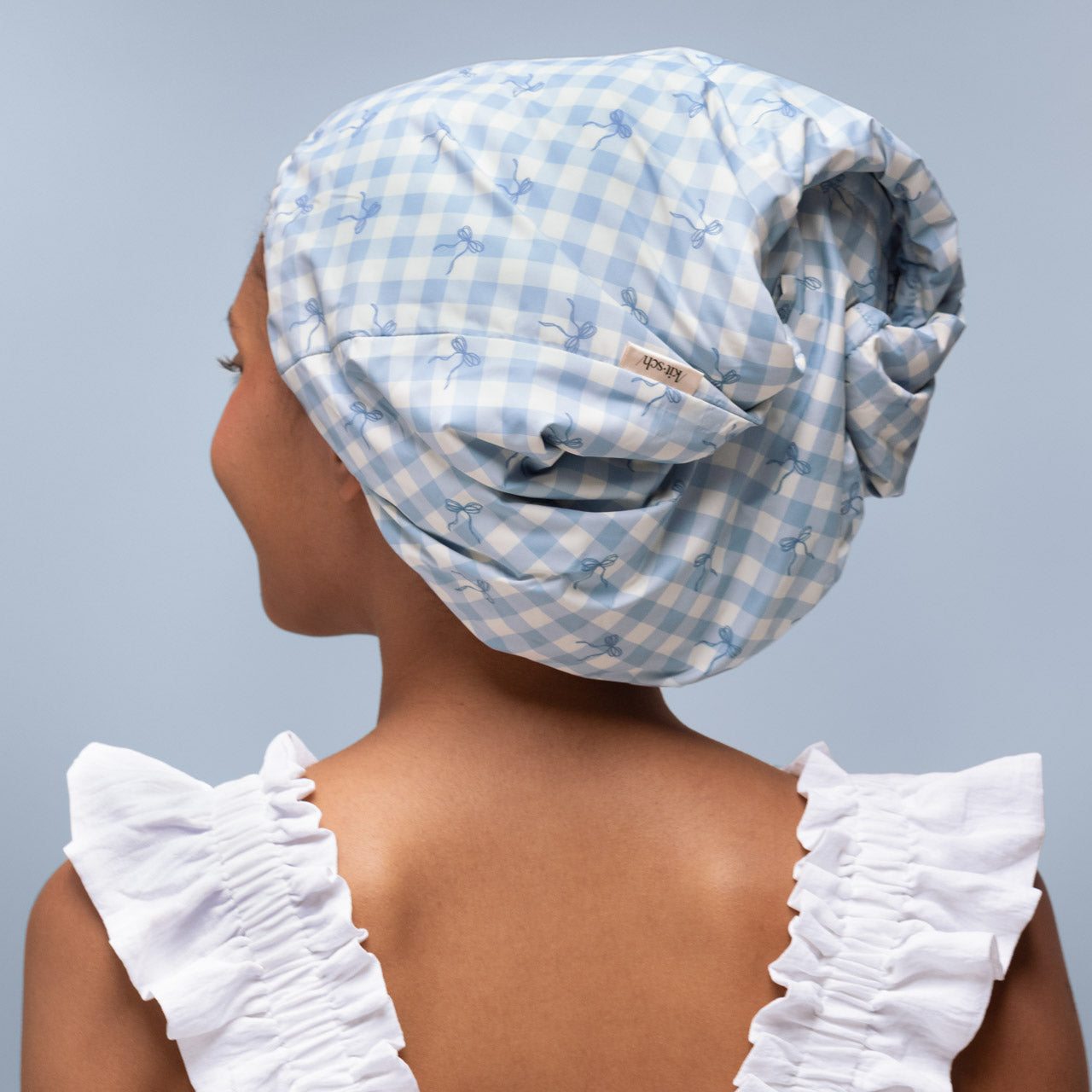 Model wearing the Kitsch Satin-Lined Flexi Shower Cap in Gingham Blue during a shower routine
