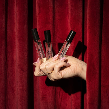 KITSCH Movie Theater Hair Perfume Trio Set — hand holding all three roller perfume bottles against red theater curtain backdrop — Buttered Popcorn, Fizzy Cola & Cinnamon Pretzel — Wear each fragrance solo or layer them together to create your own signature scent — Spritz on your hair, body & even your Kitsch Satin Pillowcase — Sheer, versatile & easy to use