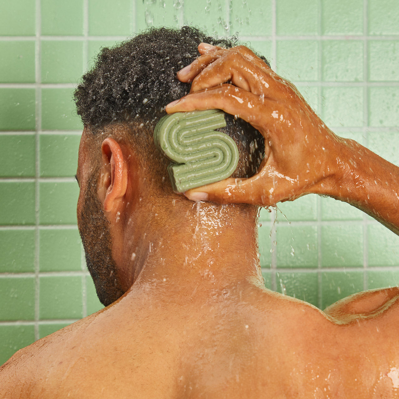 Person applying KITSCH Tea Tree & Mint Clarifying Solid Shampoo Bar directly to wet scalp in shower against green tile — sulfate-free clarifying shampoo bar that detoxes buildup, reduces oiliness, and balances scalp microbiome with Dandrilys® and tea tree & mint blend
