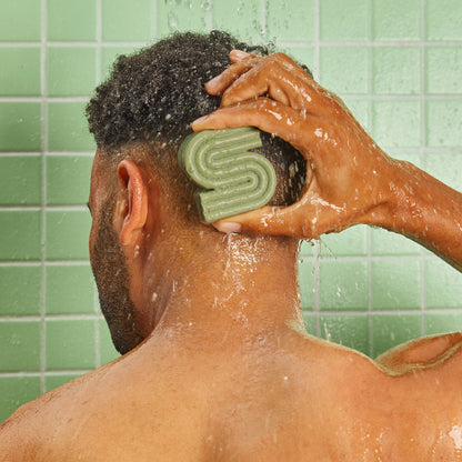 Person applying KITSCH Tea Tree & Mint Clarifying Solid Shampoo Bar directly to wet scalp in shower against green tile — sulfate-free clarifying shampoo bar that detoxes buildup, reduces oiliness, and balances scalp microbiome with Dandrilys® and tea tree & mint blend
