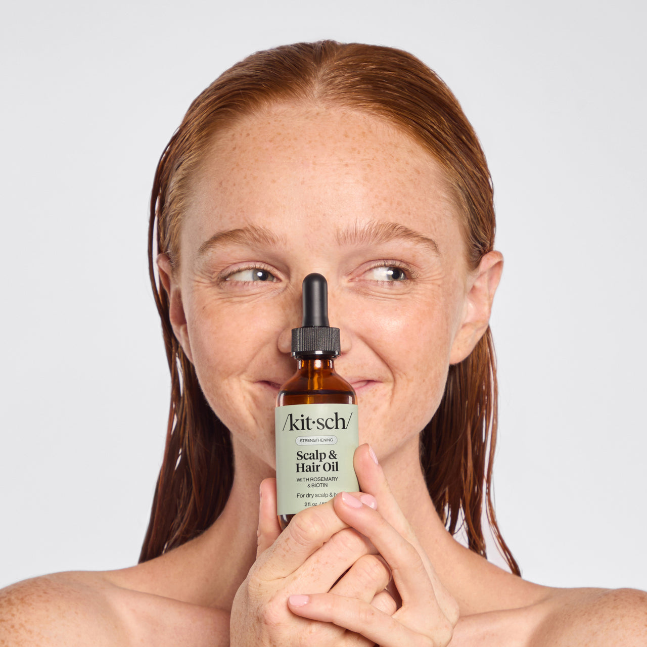 Model applying KITSCH Strengthening Rosemary & Biotin Scalp & Hair Oil with dropper to sectioned hair — supports scalp health and hair strength from root to tip — 100% plant-based formula