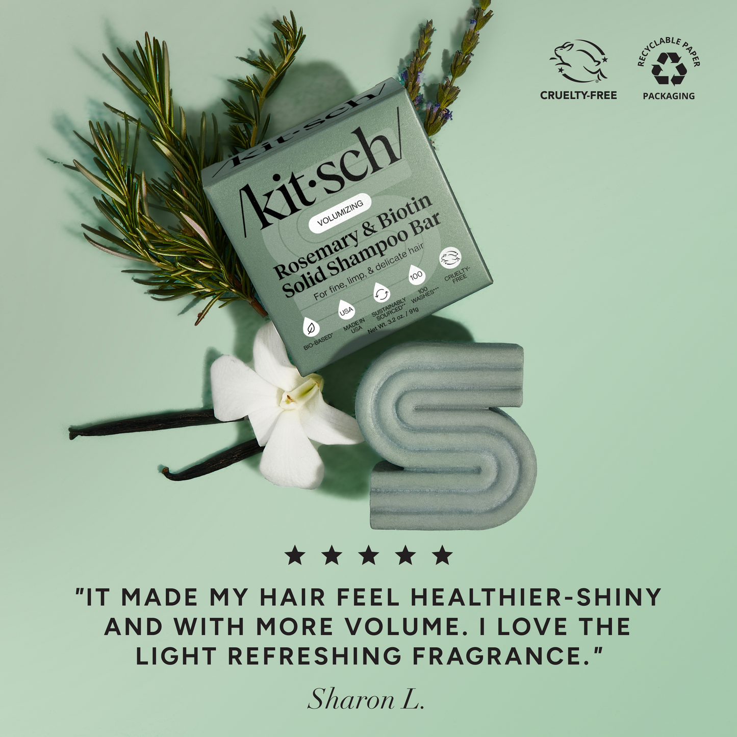 5-star customer review flat-lay for KITSCH Volumizing Rosemary & Biotin Solid Shampoo Bar on light green background styled with rosemary sprigs, white flower, and vanilla beans — Sharon L.: "IT MADE MY HAIR FEEL HEALTHIER-SHINY AND WITH MORE VOLUME. I LOVE THE LIGHT REFRESHING FRAGRANCE." — Cruelty-Free, Recyclable Paper Packaging