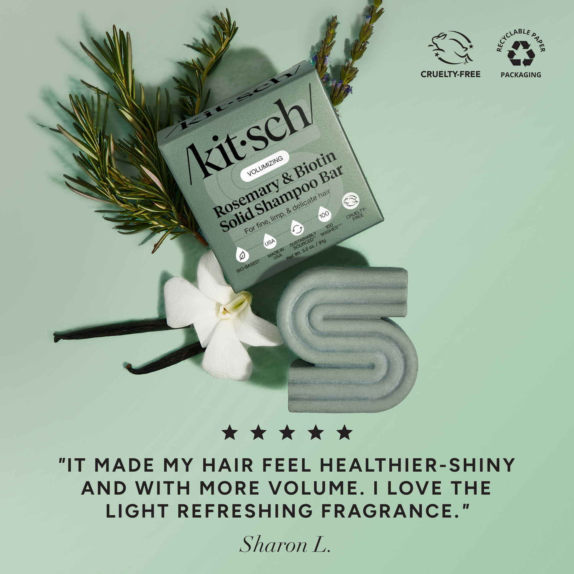 5-star customer review flat-lay for KITSCH Volumizing Rosemary & Biotin Solid Shampoo Bar on light green background styled with rosemary sprigs, white flower, and vanilla beans — Sharon L.: "IT MADE MY HAIR FEEL HEALTHIER-SHINY AND WITH MORE VOLUME. I LOVE THE LIGHT REFRESHING FRAGRANCE." — Cruelty-Free, Recyclable Paper Packaging