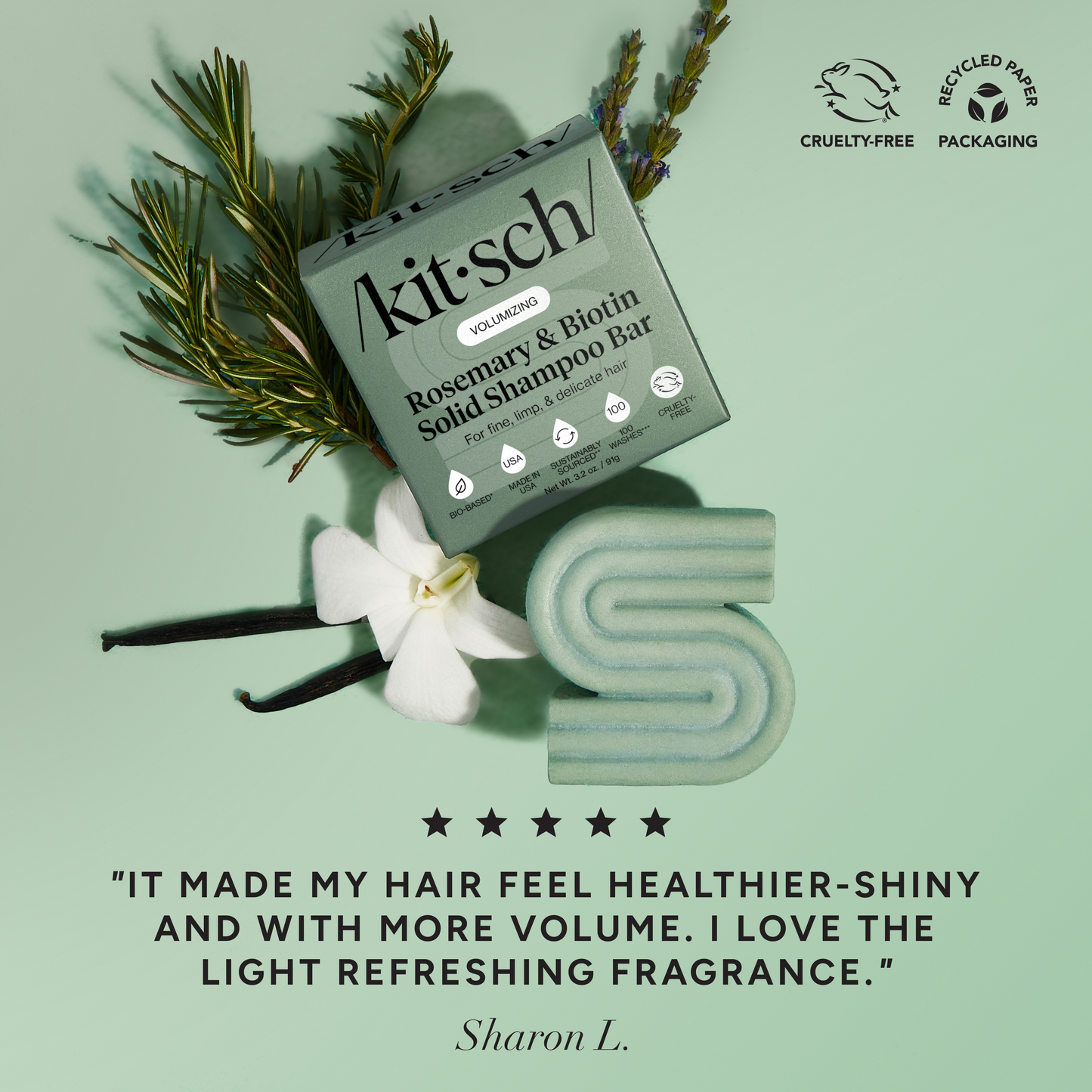 5-star customer review flat-lay for KITSCH Volumizing Rosemary & Biotin Solid Shampoo Bar on sage green background styled with rosemary sprigs, white flower, and vanilla beans — Sharon L.: "IT MADE MY HAIR FEEL HEALTHIER-SHINY AND WITH MORE VOLUME. I LOVE THE LIGHT REFRESHING FRAGRANCE." — Cruelty-Free, Recycled Paper Packaging