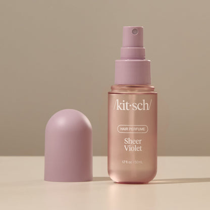 Kitsch Sheer Violet Hair Perfume bottle held by a hand against a soft warm background