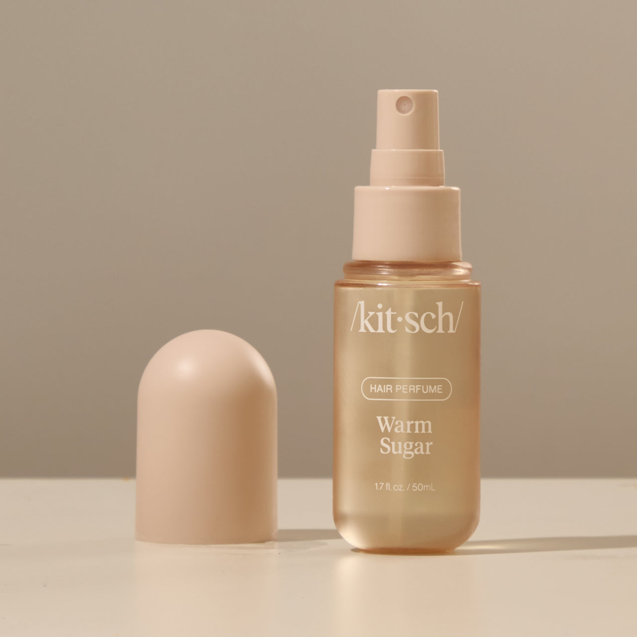 Kitsch Warm Sugar Hair Perfume bottle held by a hand against a warm neutral background