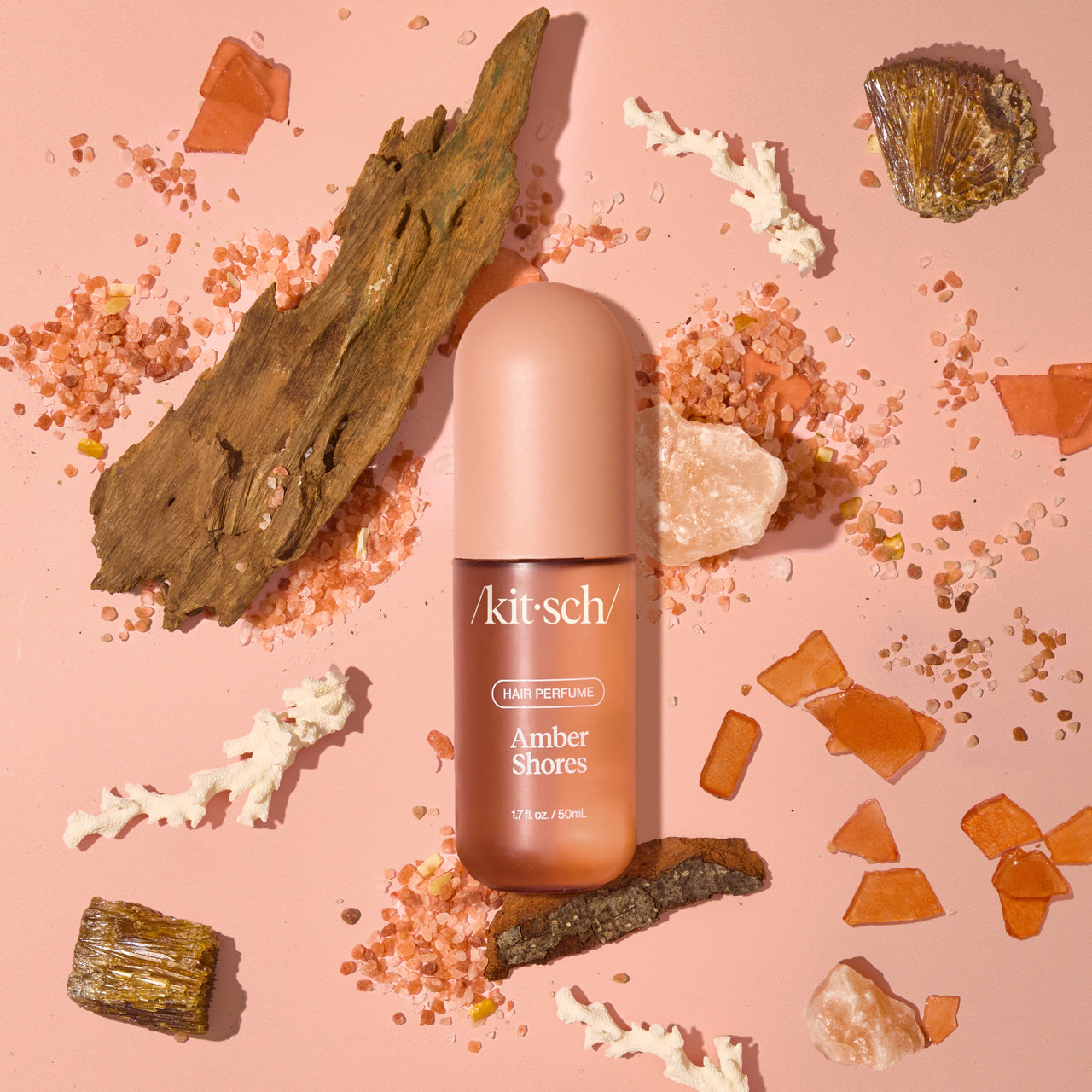 Model misting Kitsch Amber Shores Hair Perfume onto long, wavy hair