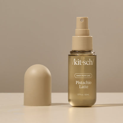 Kitsch Pistachio Latte Hair Perfume bottle held by a hand against a warm neutral background