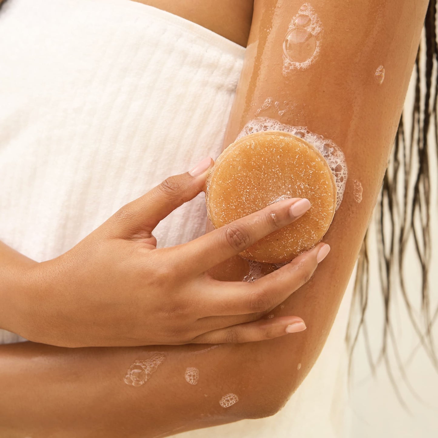 A model is using the Kitsch Exfoliating Sugar Body Scrub Bar on their leg during a shower for gentle exfoliation.